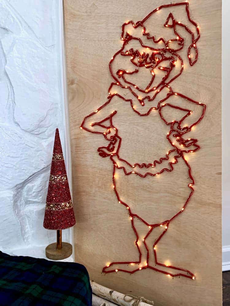 a lit grinch shape made with string and LED fairy lights on a plywood board