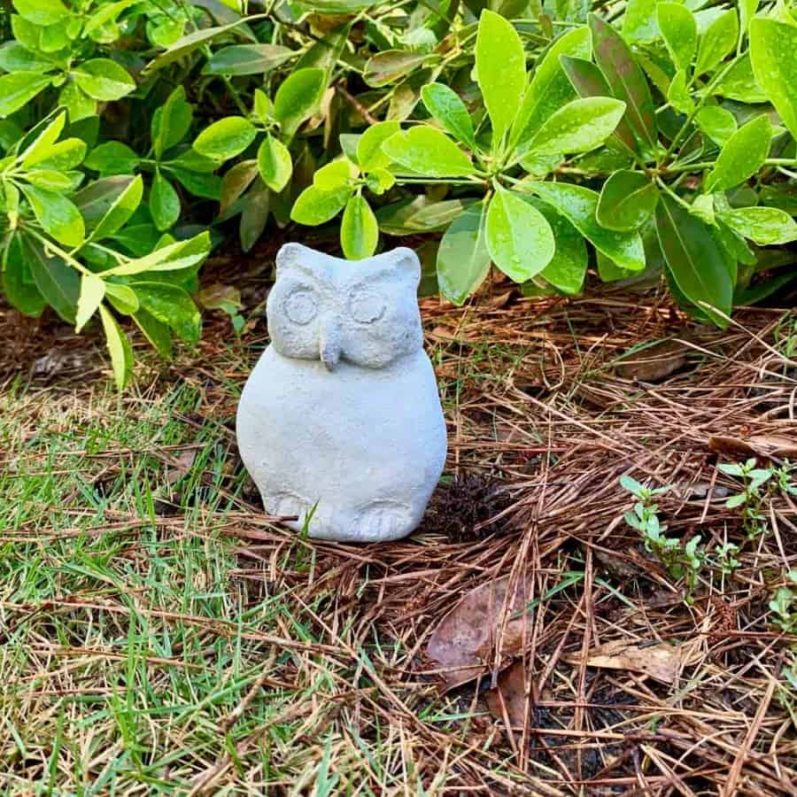 concrete garden owl statue in front of bushes