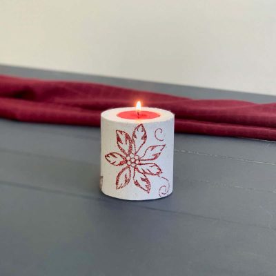 concrete candle on blue wood planks with red background. candle has poinsettia design