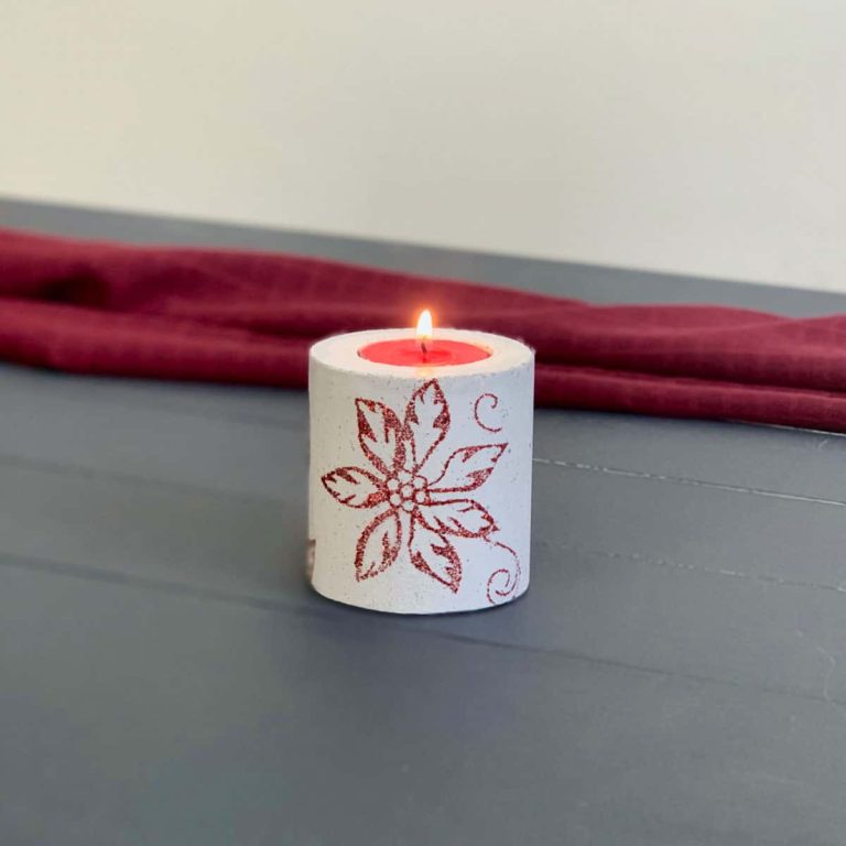 concrete candle on blue wood planks with red background. candle has poinsettia design