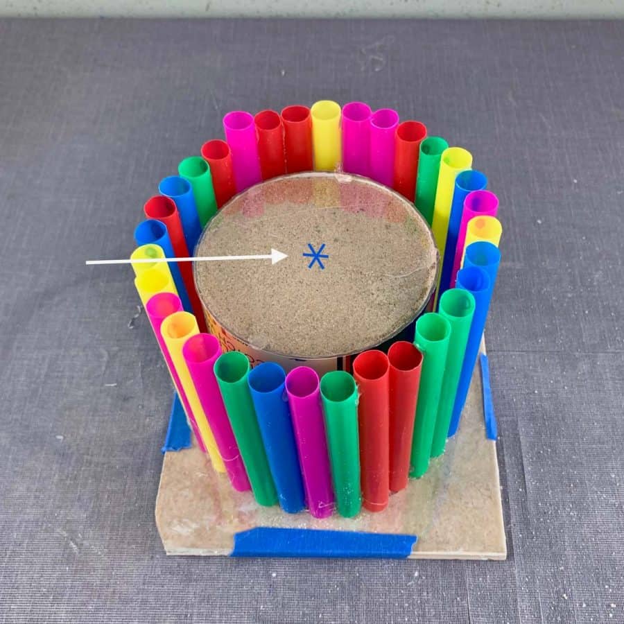 criss cross mark on top of sand-filled inner mold of concrete planter with straws in circle.