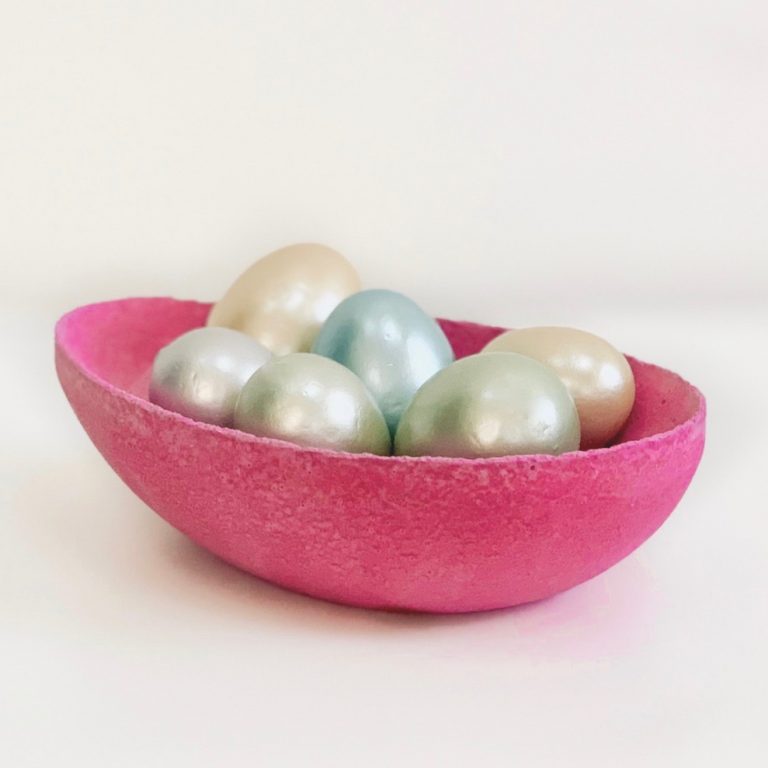 dark pink colored concrete bowl with pastel colored eggs inside