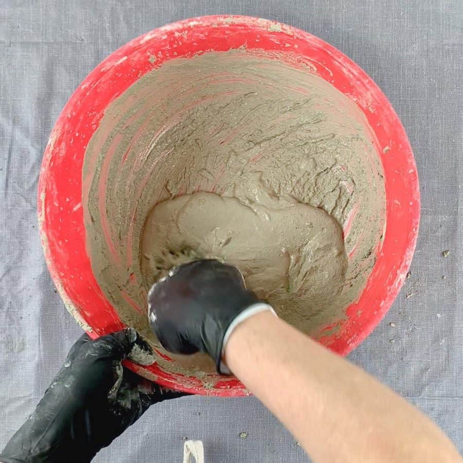 bowl of wet cement being mixed with gloved hands