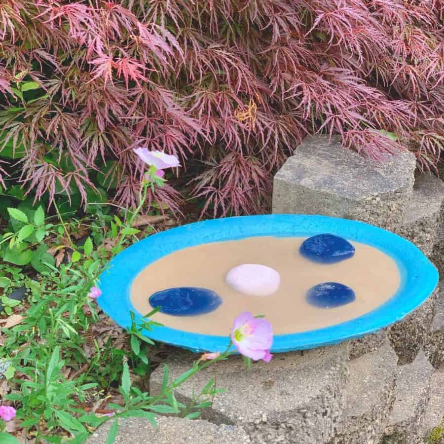 shallow concrete tray with sand, water and rocks. Painted a teal color. Sitting in a garden.