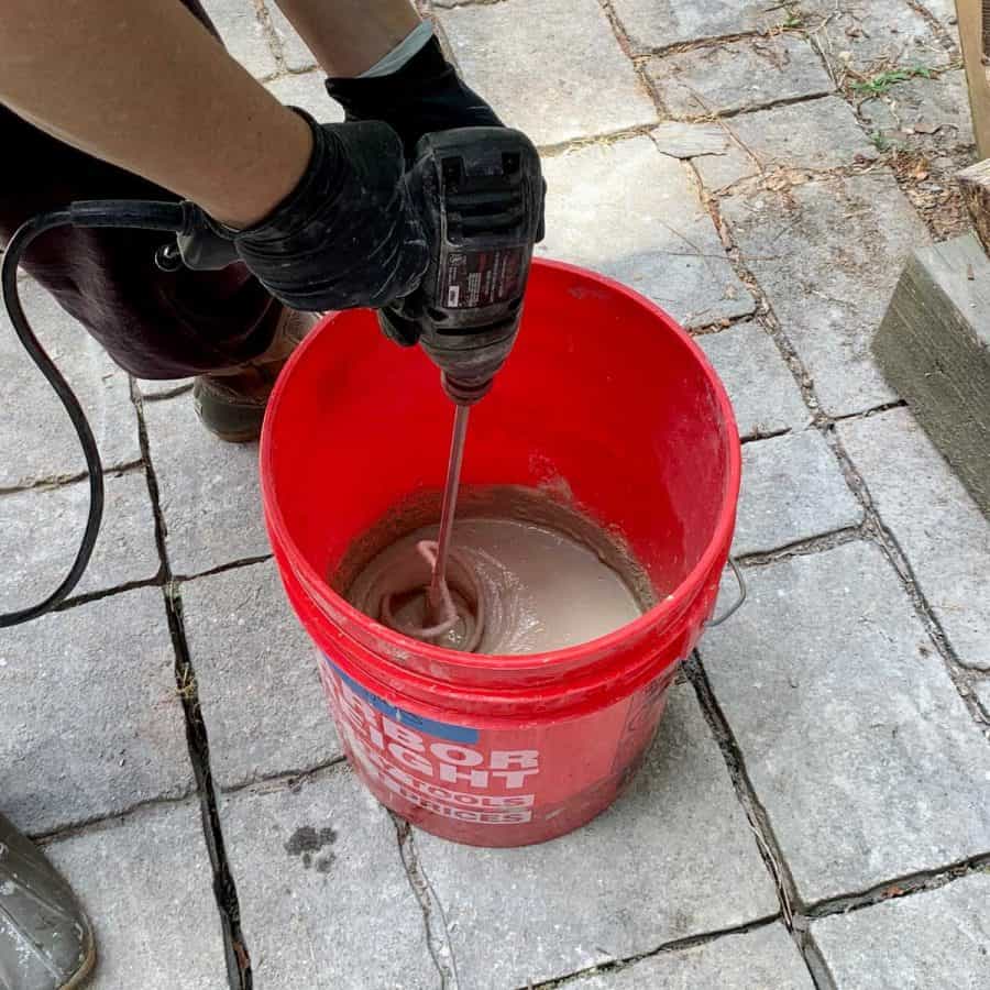 level concrete floor- person holding drill with longer paddle mixer attachment, mixing wet concrete leveling mix inside of bucket