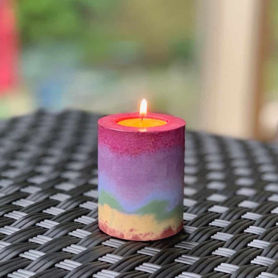 Concrete Candle Holder-layers of rainbow colors in a concrete candle holder, on a table. Tealight candle inside is lit.