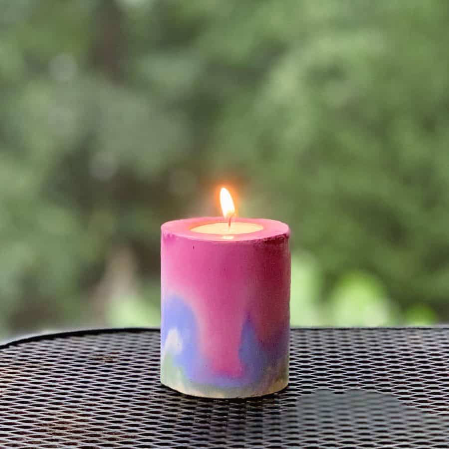 Concrete Candle Holder-layers of rainbow colors in a concrete candle holder, on a table. Tealight candle inside is lit.