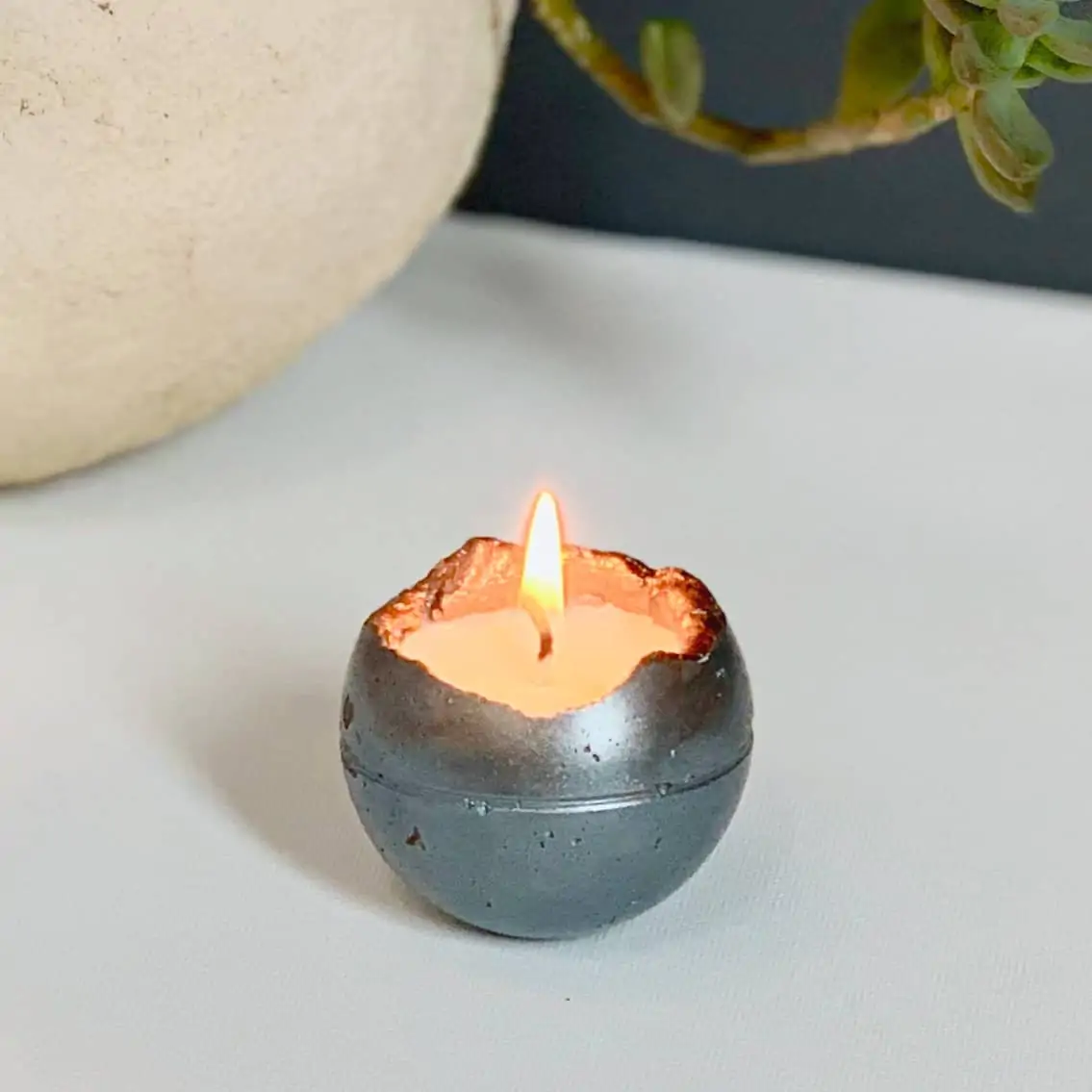 concrete candle- metallic blue and copper colored round candle made of concrete is lit on table