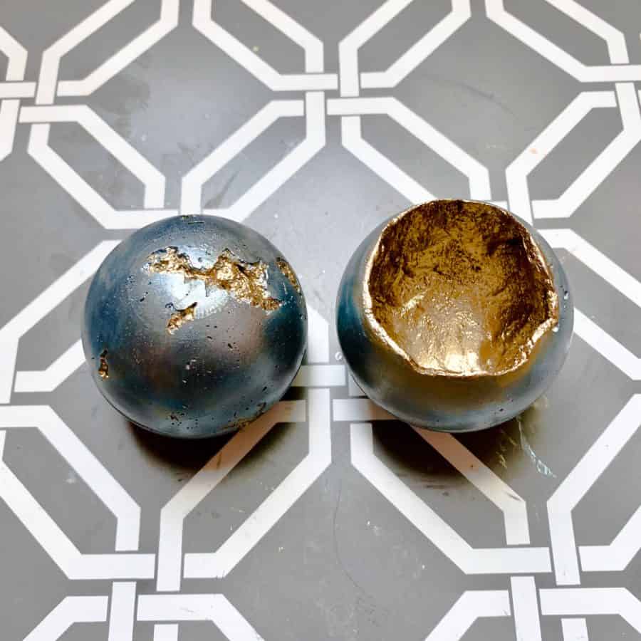 concrete candle- two candle vessels one upside down with pitting showing gold inside the rest of ball is blue. Inside of other ball is gold.