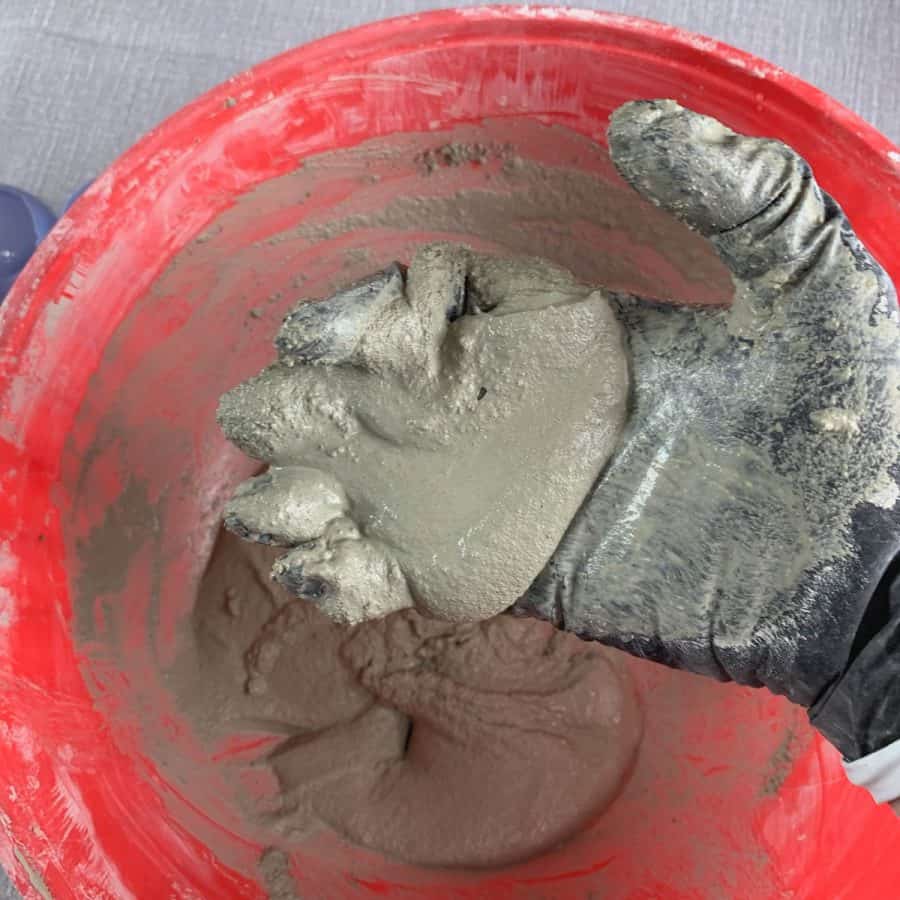 concrete candle- wet cement mixture in hand above mixing bowl