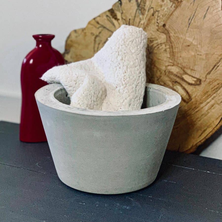 large diy concrete bowl with soft sherpa baby blanket rolled up inside against wood backdrop next to vase