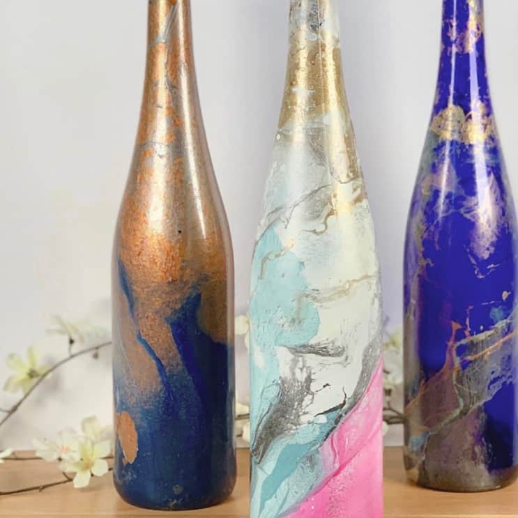 3 diy hydro dipped bottles on table with white flowers
