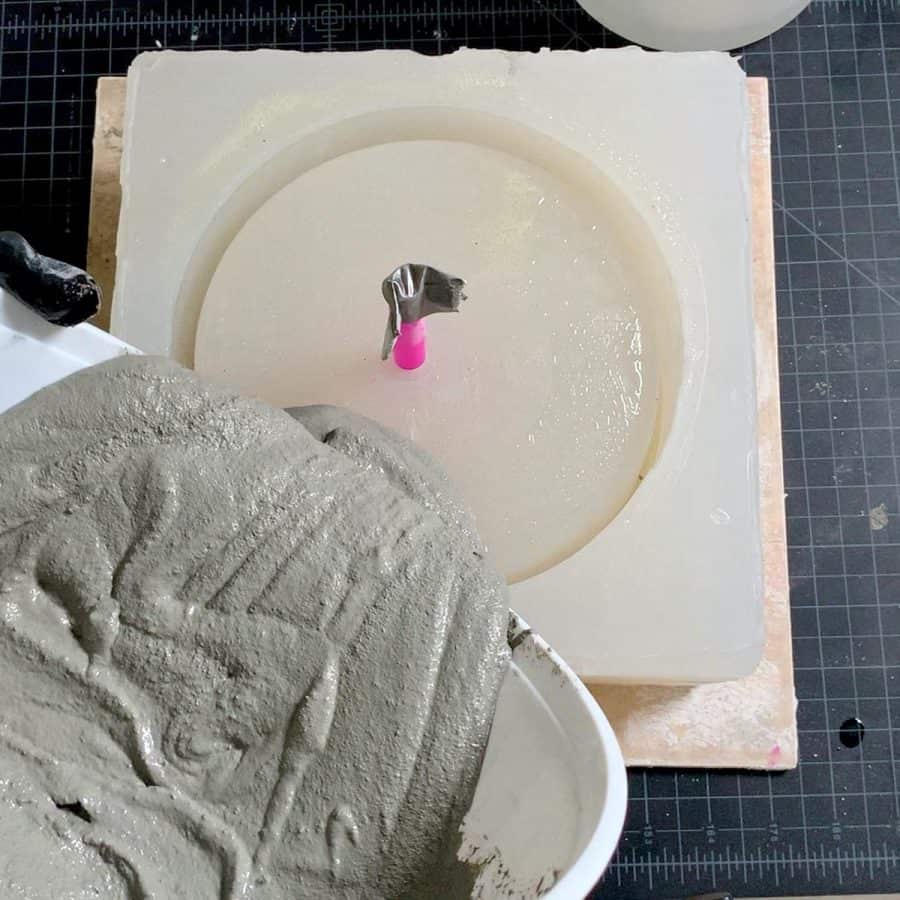 bowl above large concrete silicone mold with wet cocnrete mixture flowing into mold
