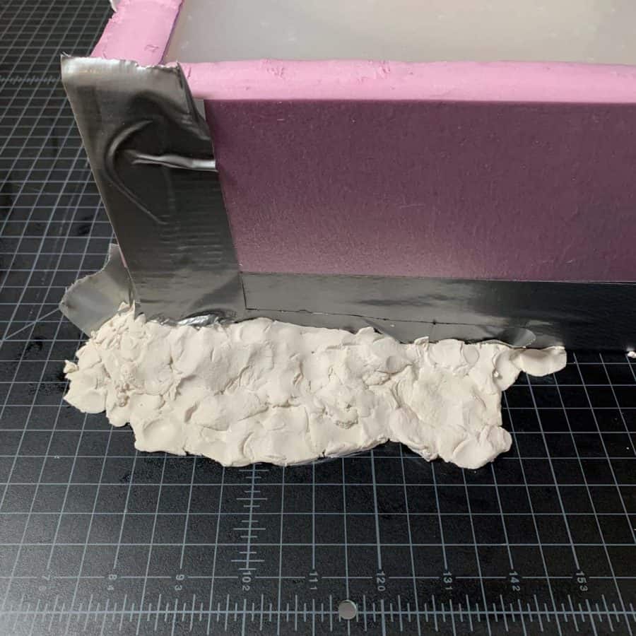 clay packed up around bottom edge and corner of silicone mold box