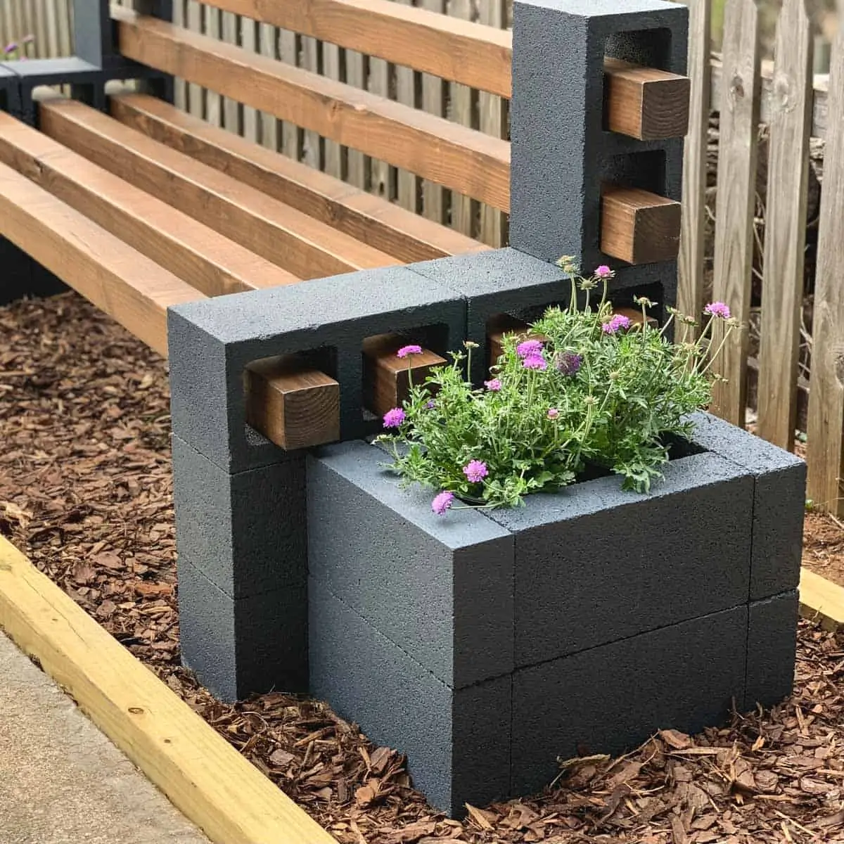 blue planter box made with concrete blocks butting up against wood and cinder block bench. Has purple flowers inside.