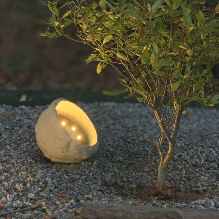 solar light inside of rock made from concrete, lighting up a tree at nighttime