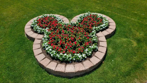 A flower bed lined with brick pavers and is in the shape of mickey mouse's head. Bed is filled with flowers.