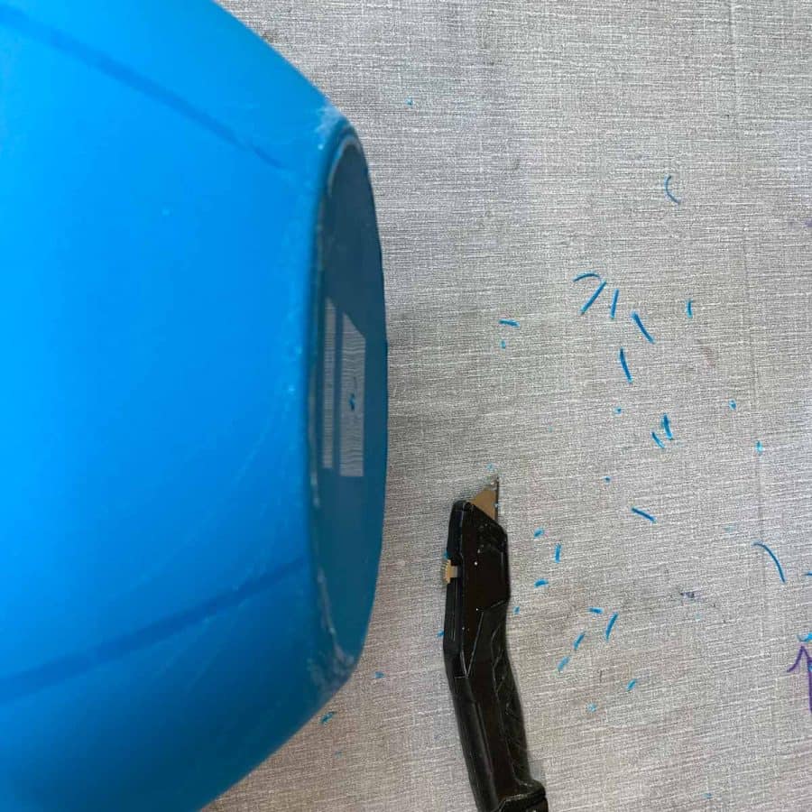the bottom of a plastic bowl next to a utility knife with pieces of plastic shavings next to it on table