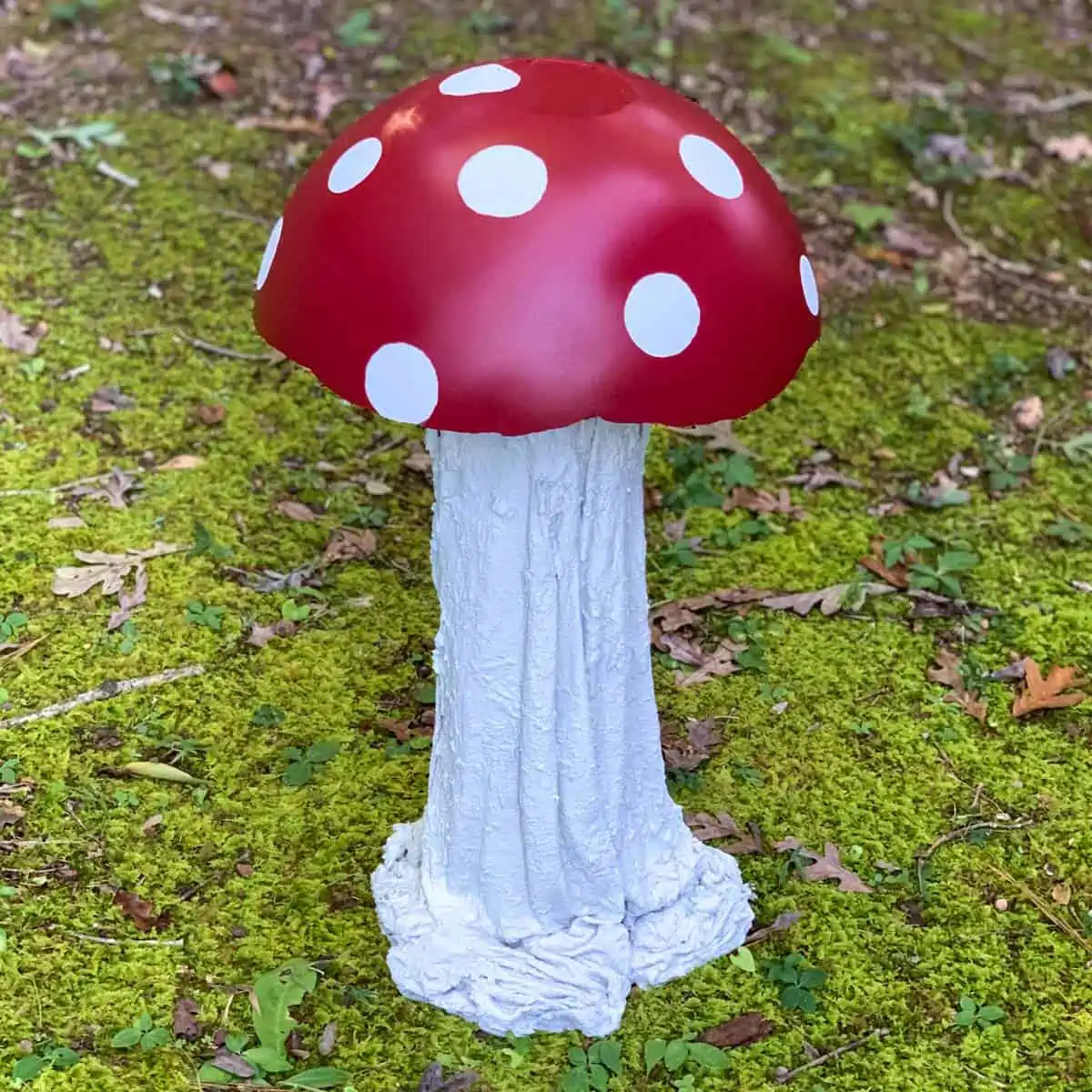 a mushroom made from concrete on a mossy lawn. the cap is red with white spots.