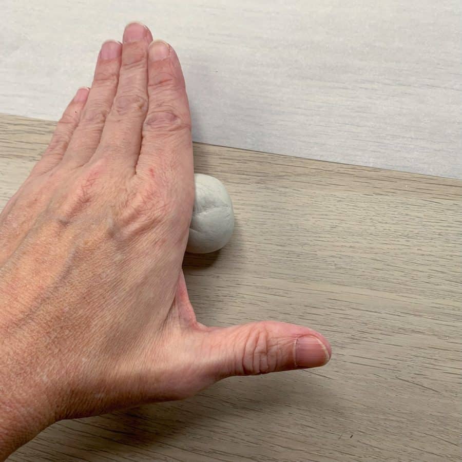 hand on top of clay ball, rolling it on a table