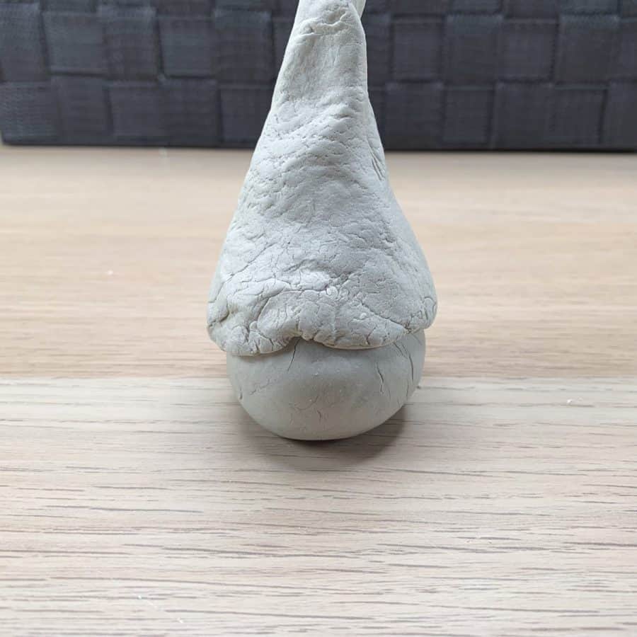 clay gnome standing up with hat and middle of hat is pushed up where nose goes.