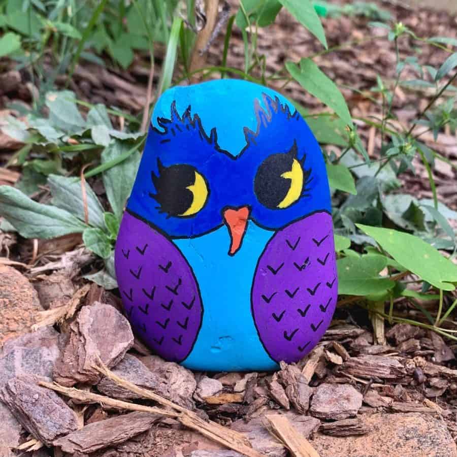 finished owl rock painting sitting in a garden area