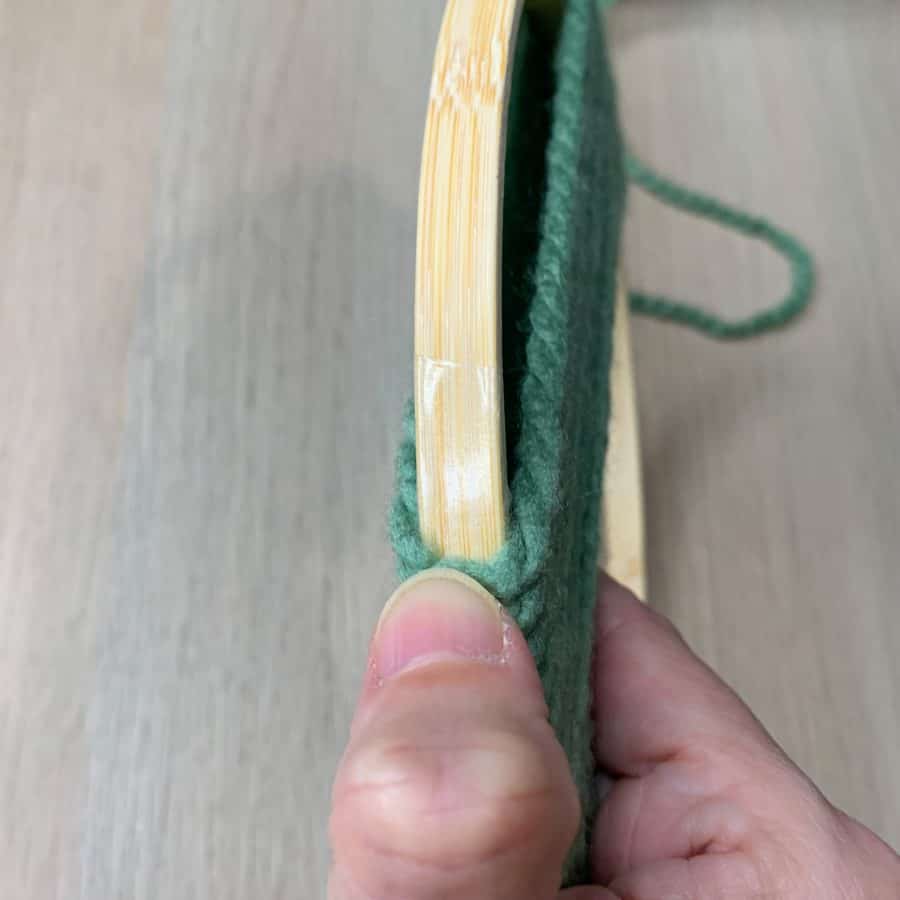 thumb holding yarn to side of ring that has double-sided tape attached to it.