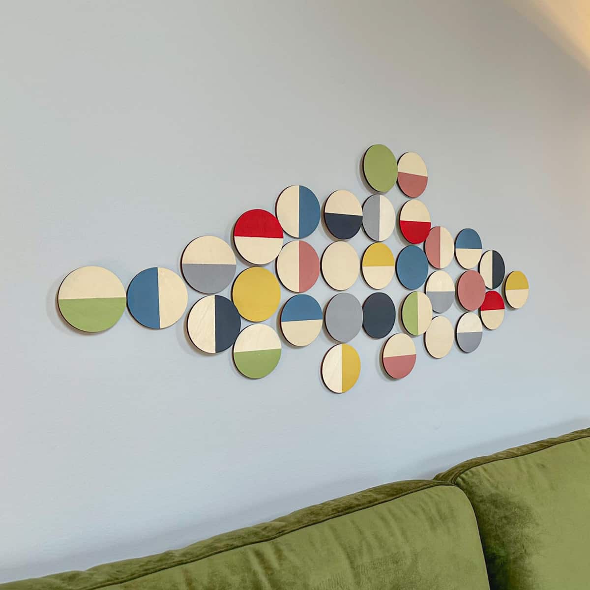 round wood discs on wall painted with mid century modern colors in a geometric pattern, displayed as wall art over sofa.