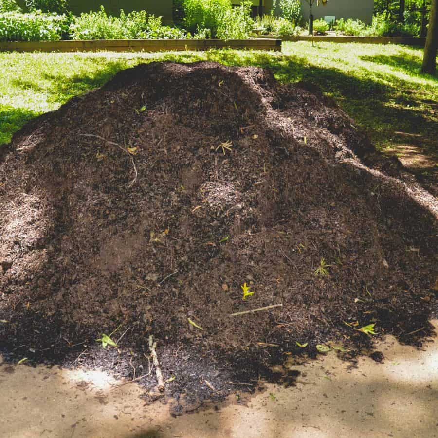 A large pile of bulk soil or compost material on a driveway.