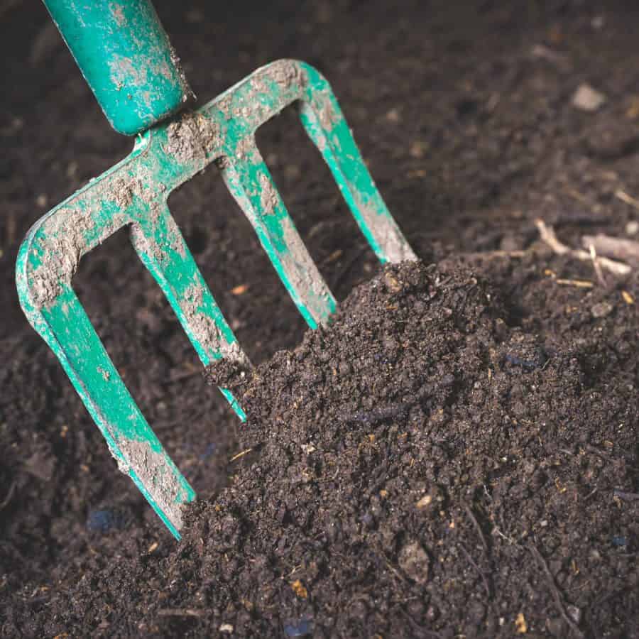 A garden hoe digging into a pile of composted soil.