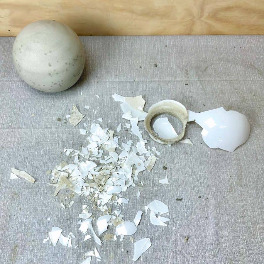 A DIY concrete ball next to many shards of glass from the globe light fixture.