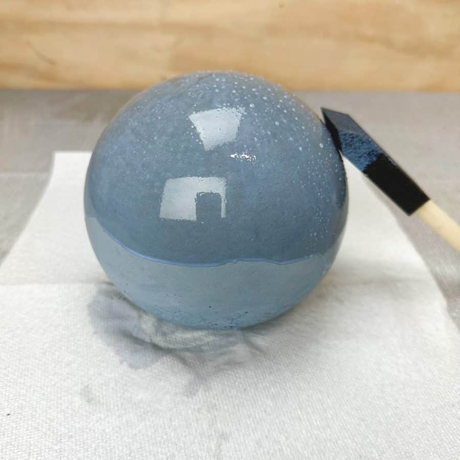 Wet wood stain being applied to grey DIY concrete sphere.