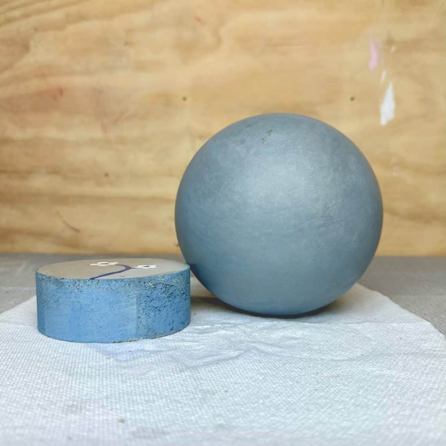 Finished, sealed blue concrete sphere next to other blue concrete piece. Other concrete piece shows slightly more saturated and brighter blue color.