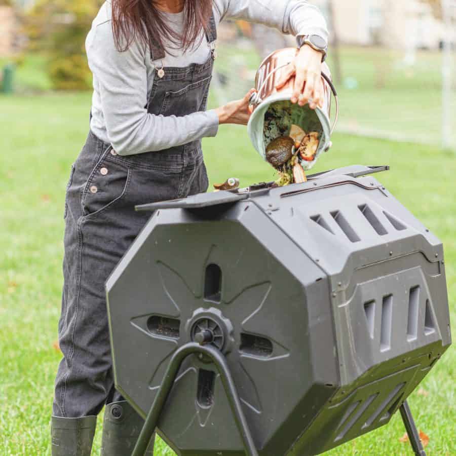 A woman pouring organic scraps into a plastic barrel that is sideways on a frame before it gets turned with a handle.