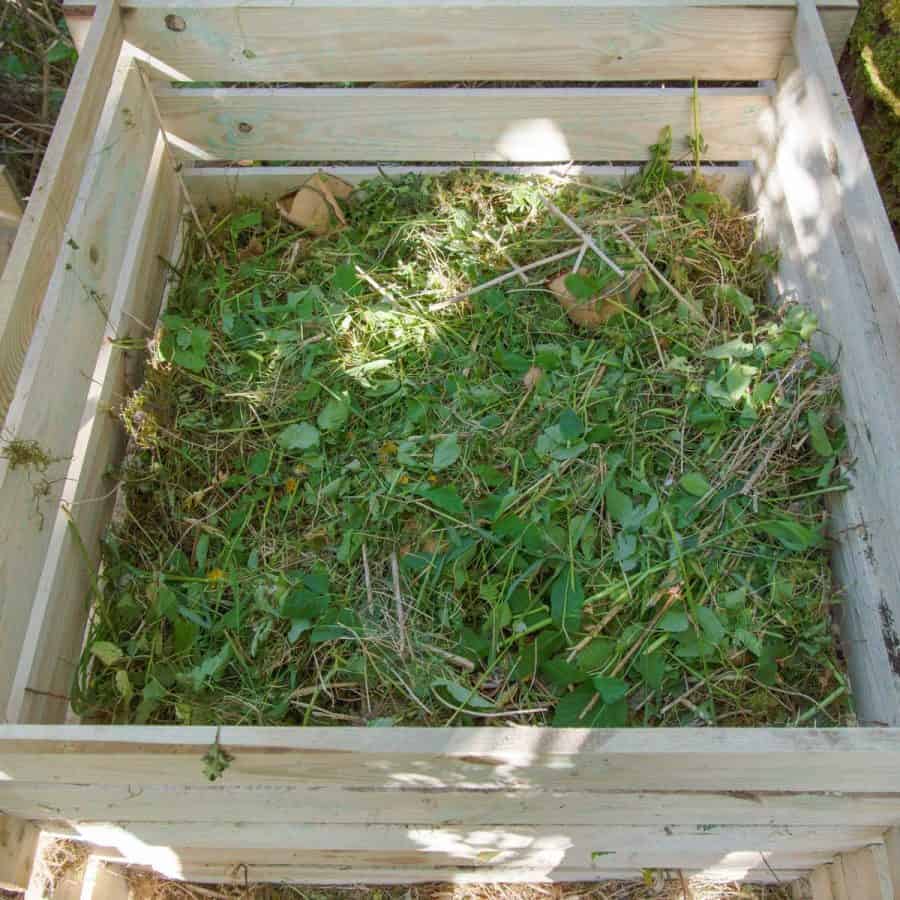 A large wood bin filled with yard waste like grass clippings, leaves and weeds.