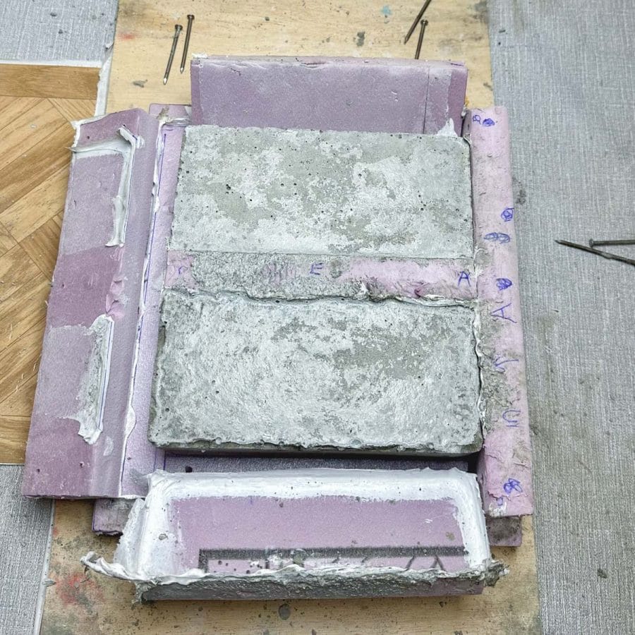 Cured concrete bricks inside mold with 2 sides peeled back.