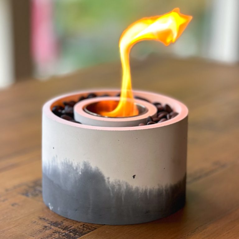 a black and white marbled-looking concrete bowl on a tabletop with a flame coming out of it, sitting on a table outside.