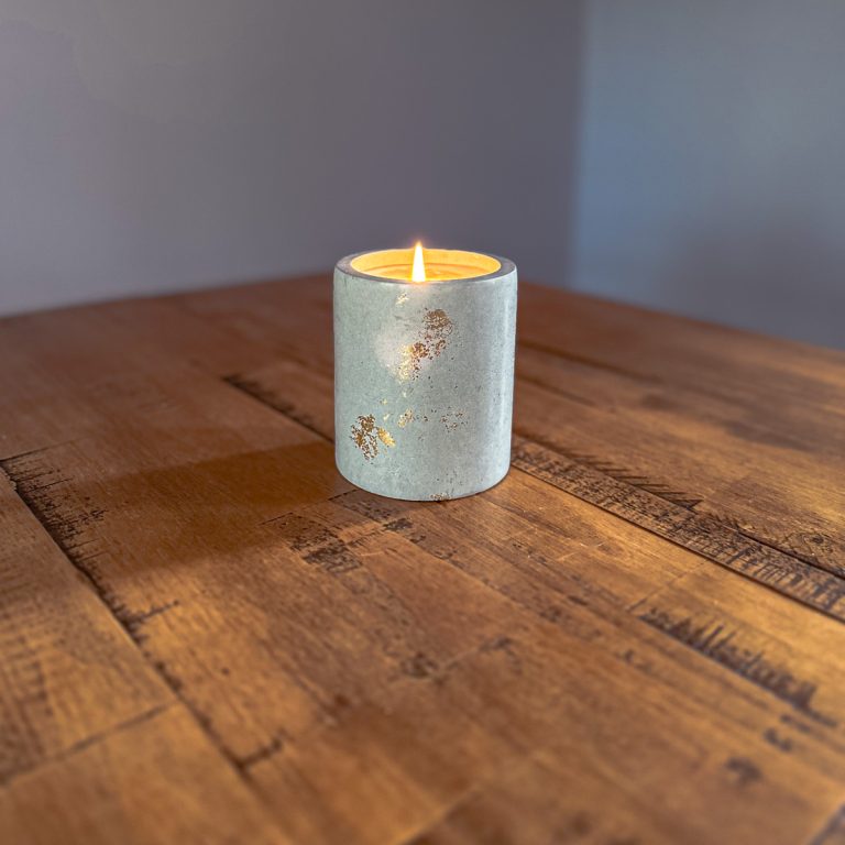 A lit concrete candle jar on a table.