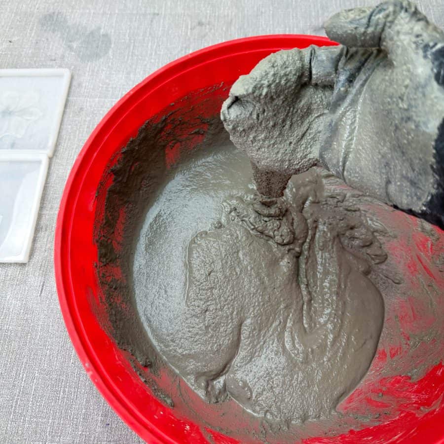 A hand holding cement mixture that is flowing from it into a bowl.