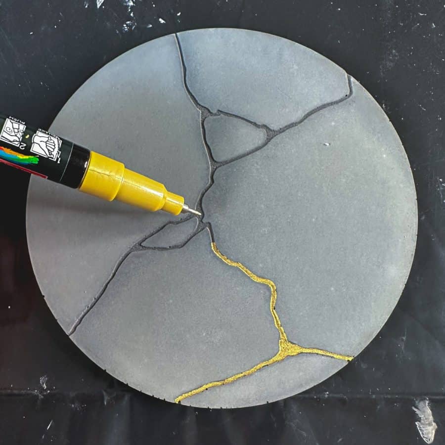 gold paint pen drawing in golden lines into kintsugi concrete coater.