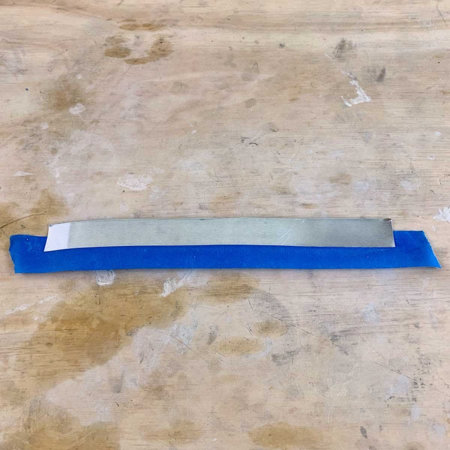a piece of aluminum cut into a rectangle with blue tape along the long edge