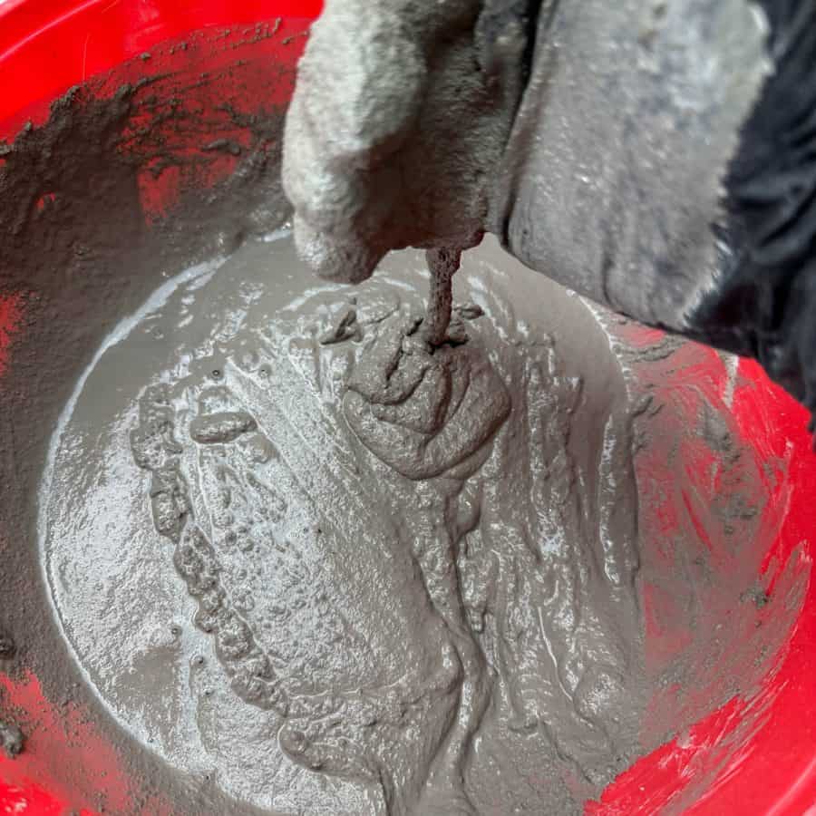 A hand with cement mixture flowing into bowl showing correct water to cement ratio for crafts.