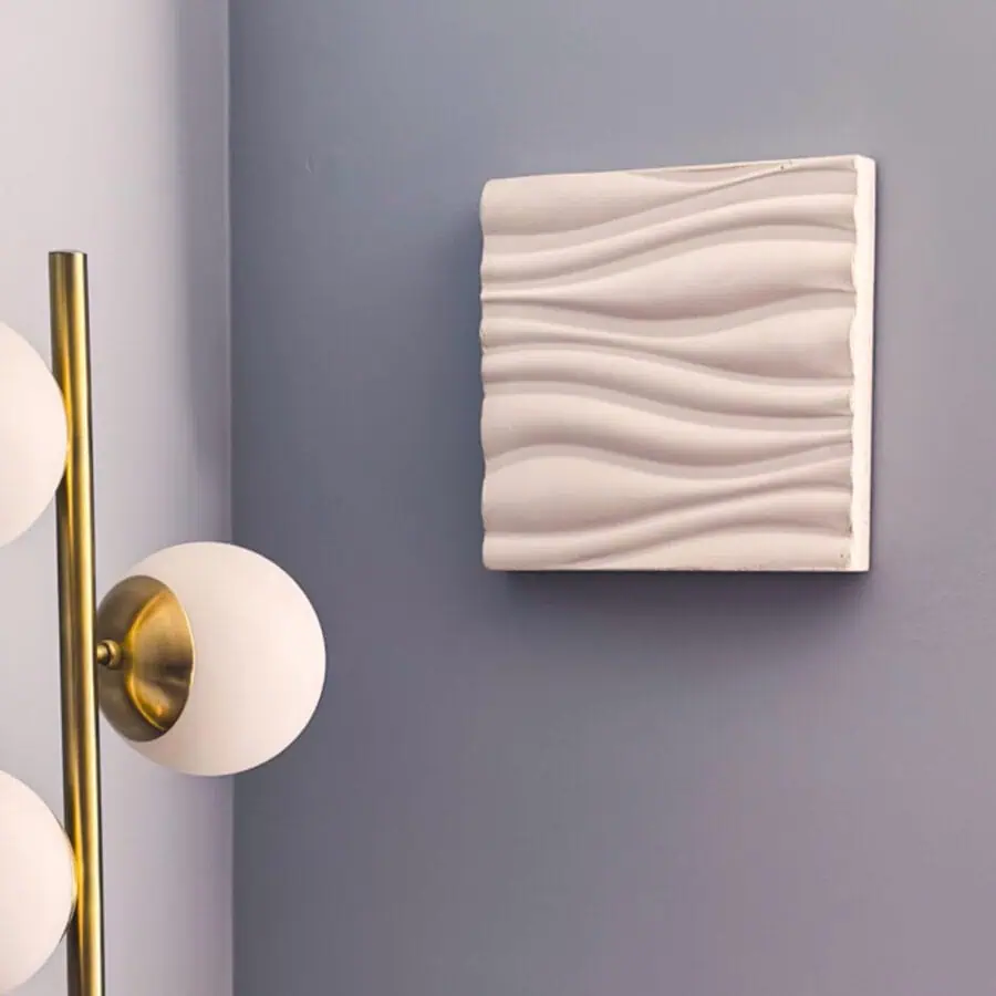 A piece of white cement wall art with three dimensional waves on a wall.